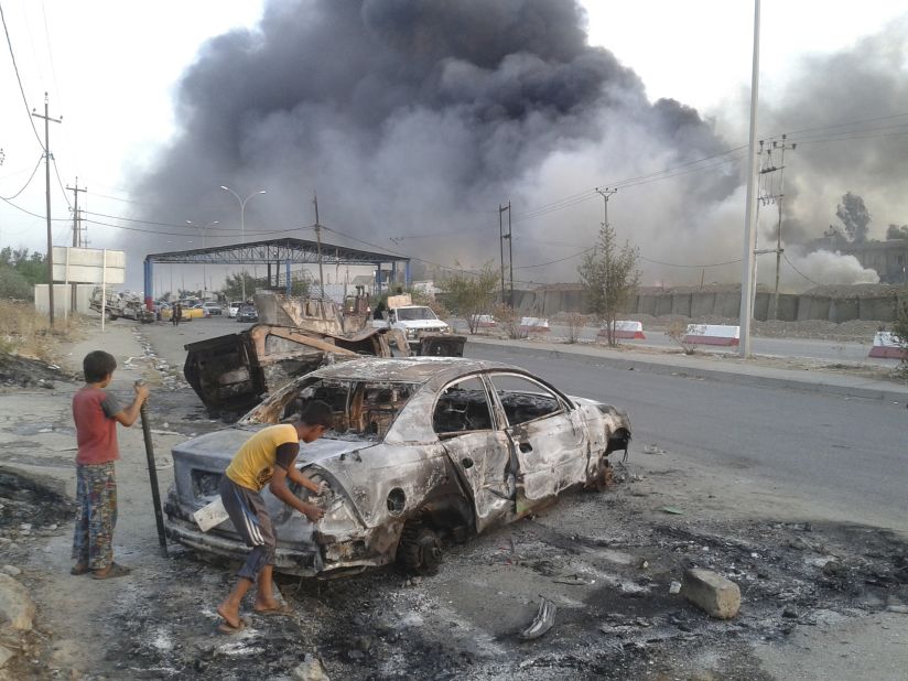 Children stand next to a burnt vehicle during clashes between Iraqi security forces and ISIS militants in Mosul on Tuesday, June 10.