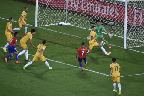 Chile forward Alexis Sanchez kicks the ball past two Australians to score the opening goal of the match.
