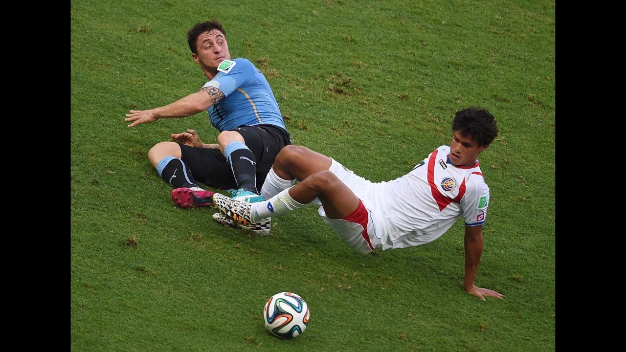 Uruguay midfielder Cristian Rodriguez, left,  falls to the ground with Costa Rica counterpart Yeltsin Tejeda.