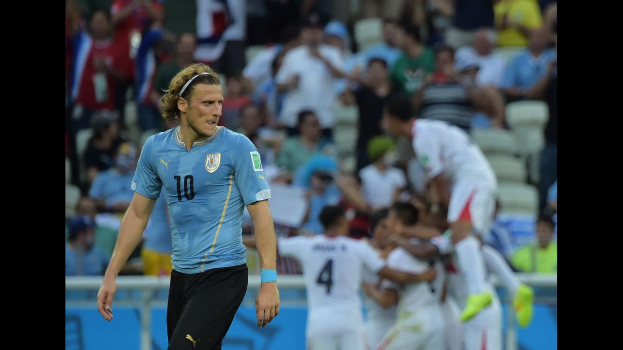 Uruguay forward Diego Forlan looks rueful as Costa Rica's players celebrate a goal in the background.