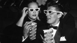 November 1952:  EXCLUSIVE American actor Keefe Brasselle and his wife Norma, wearing 3-D glasses and holding boxes of hot buttered popcorn, sit in the theater at the premiere of director Arch Oboler's film, 'Bwana Devil,' Hollywood, California. The film was the first commercial 3-D feature. In the background American actor Charles Coburn is visible.  (Photo by M. Garrett/Murray Garrett/Getty Images)