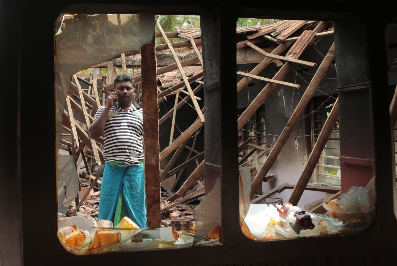 A Muslim man talks on his phone while standing in what's left of his house.