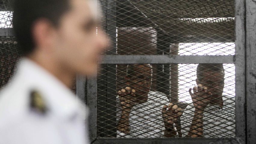 Australian journalist Peter Greste of Al-Jazeera (C) looks on standing inside the defendants cage during his trial along with 19 co-defendants for allegedly defaming the country and ties to the blacklisted Muslim Brotherhood on May 3, 2014 in the police institute near Cairo's Turah prison.