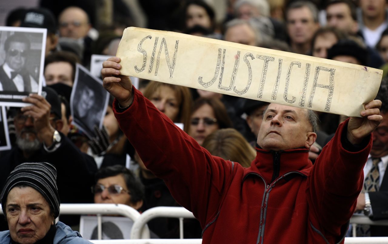 A man shows a placard that reads "Without Justice" amid people holding portraits of victims of the terrorist bombing attack on the commemoration of its 18th anniversary, in Buenos Aires on July 18, 2012. 