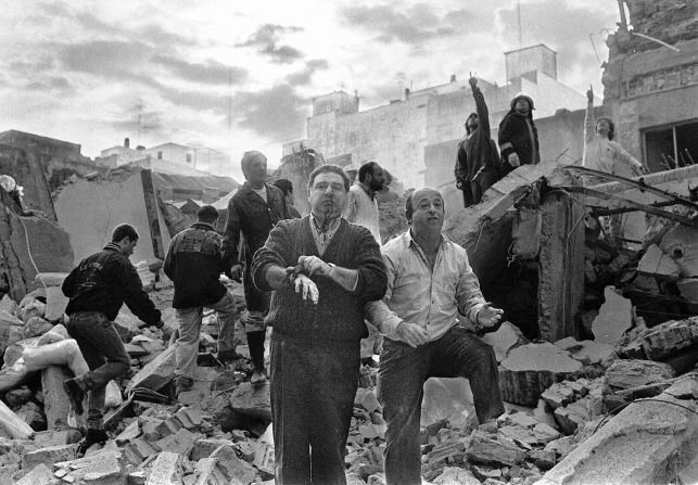 Firemen search as wounded people walk over the rubble left following the explosion.