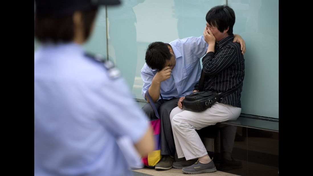 A police officer watches a couple cry outside the airline's office building in Beijing after officials refused to meet with them on June 11, 2014. The couple's son was on the plane.