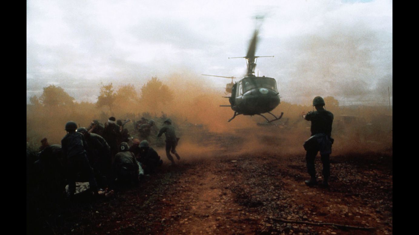 Tim Page photographed a U.S. helicopter taking off from a clearing near Du Co SF camp in Vietnam in 1965. Wounded soldiers crouch  in the dust of the departing helicopter. The military convoy was on its way to relieve the camp when it was ambushed.