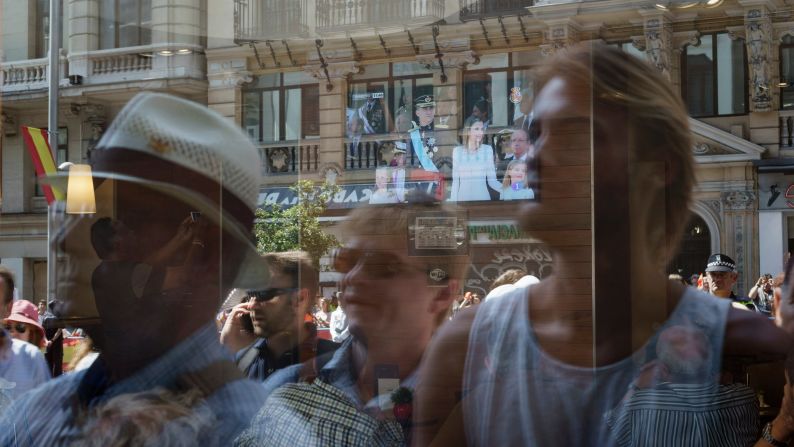 Well-wishers are reflected on a window as they gather at the royal palace.