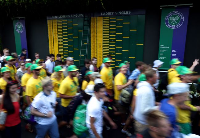 Spectators walk past the order-of-play boards at the All England Tennis Club.