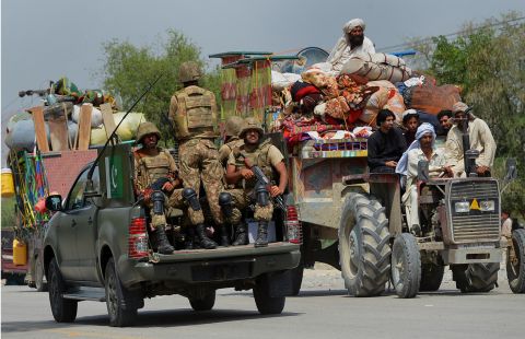 Pakistani troops patrol as displaced civilians cross a checkpoint.