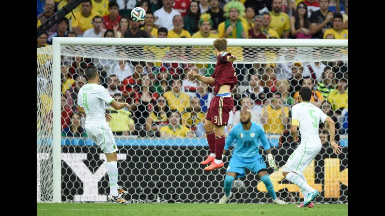 Russia forward Alexander Kokorin, center, scores his team's first goal past Algeria's goalkeeper Rais Mbohli, in blue.