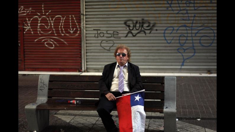 A man holding a Chilean flag sits alone on a street bench in Santiago, Chile, after Chile was defeated by Brazil and knocked out of the World Cup on Saturday, June 28.