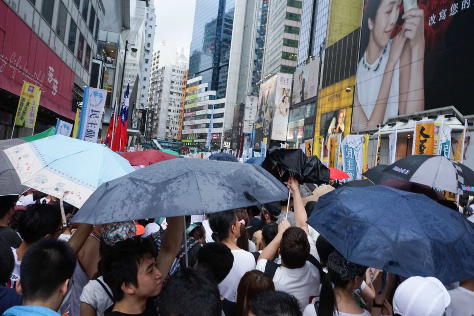 As rain begins to come down on the protesters, umbrellas fly open.