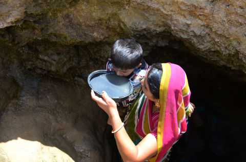 A woman offers drinking water from a well to her son in Surendranagar on June 1.