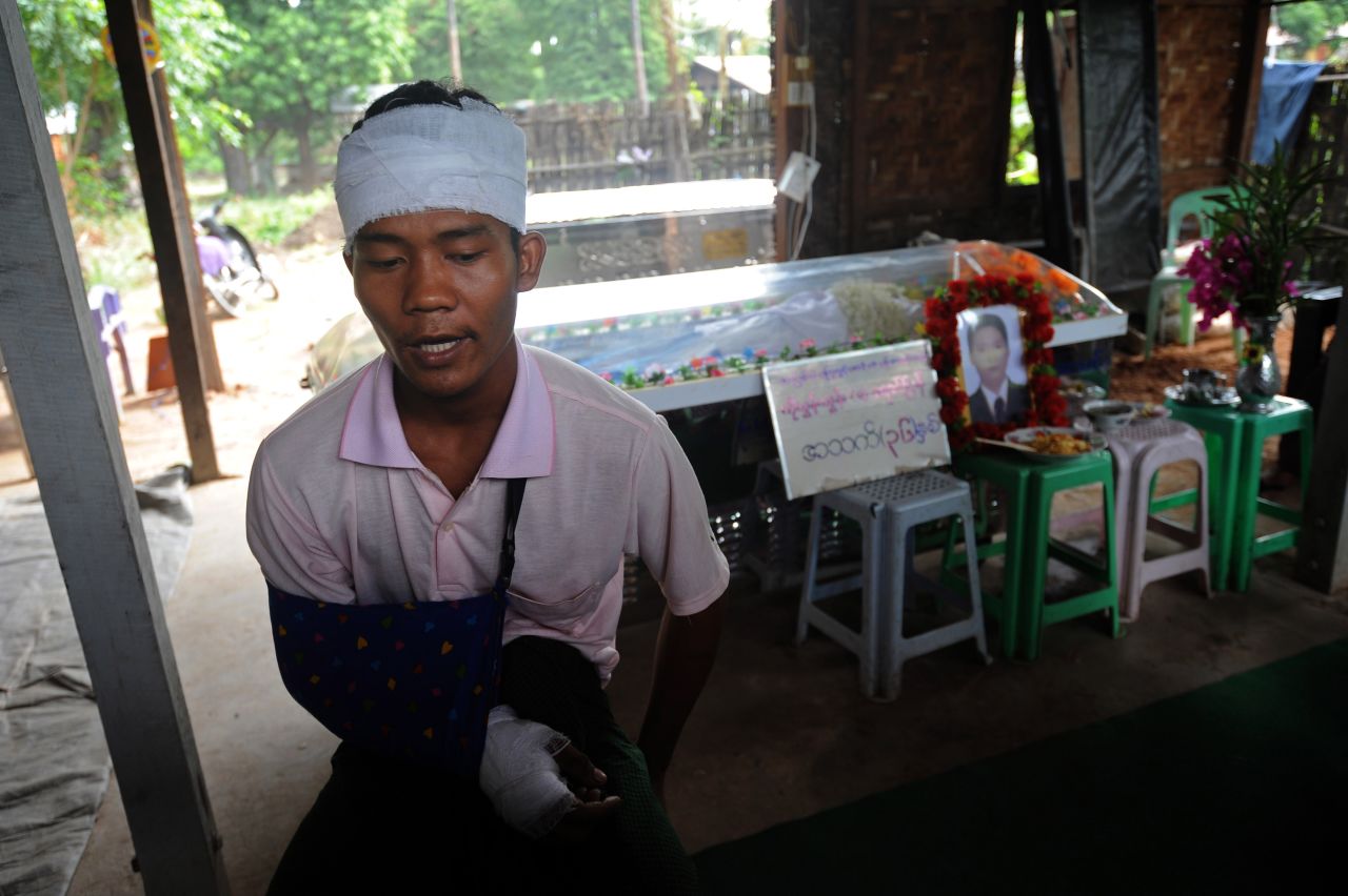 Ko Htwe, who was injured in the riots, sits next to his friend's coffin. Officials say 14 people were injured in the unrest.