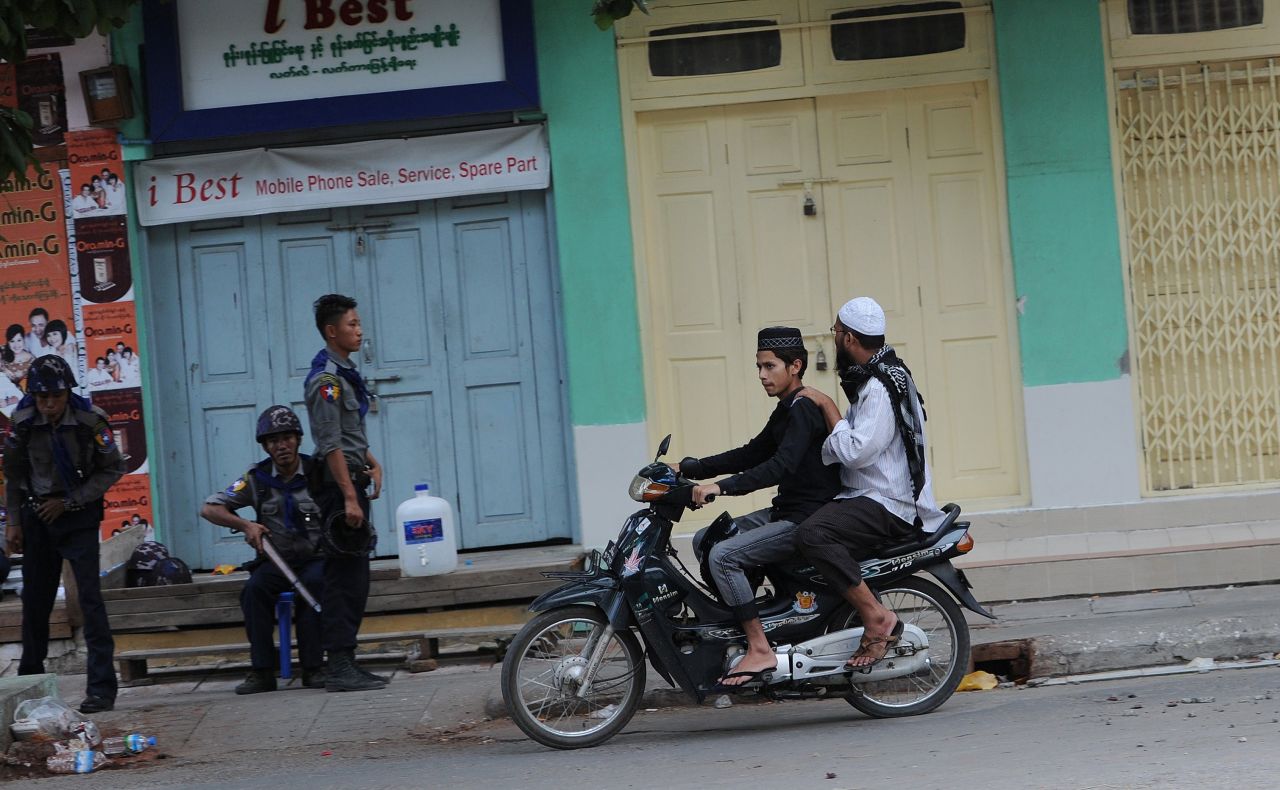 Two Muslims ride past officers imposing order in the streets of Mandalay, Myanmar's multicultural, multi-faith second city. Muslims, who comprise about 5% of Myanmar's population, have been the target of occasional mob violence at the hands of the country's Buddhist majority in recent years,