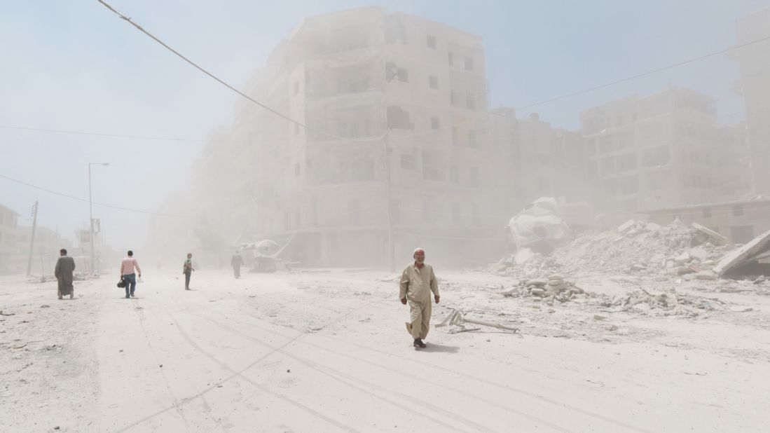 People walk on a dust-filled street after a reported barrel-bomb attack in Aleppo on Monday, July 7.