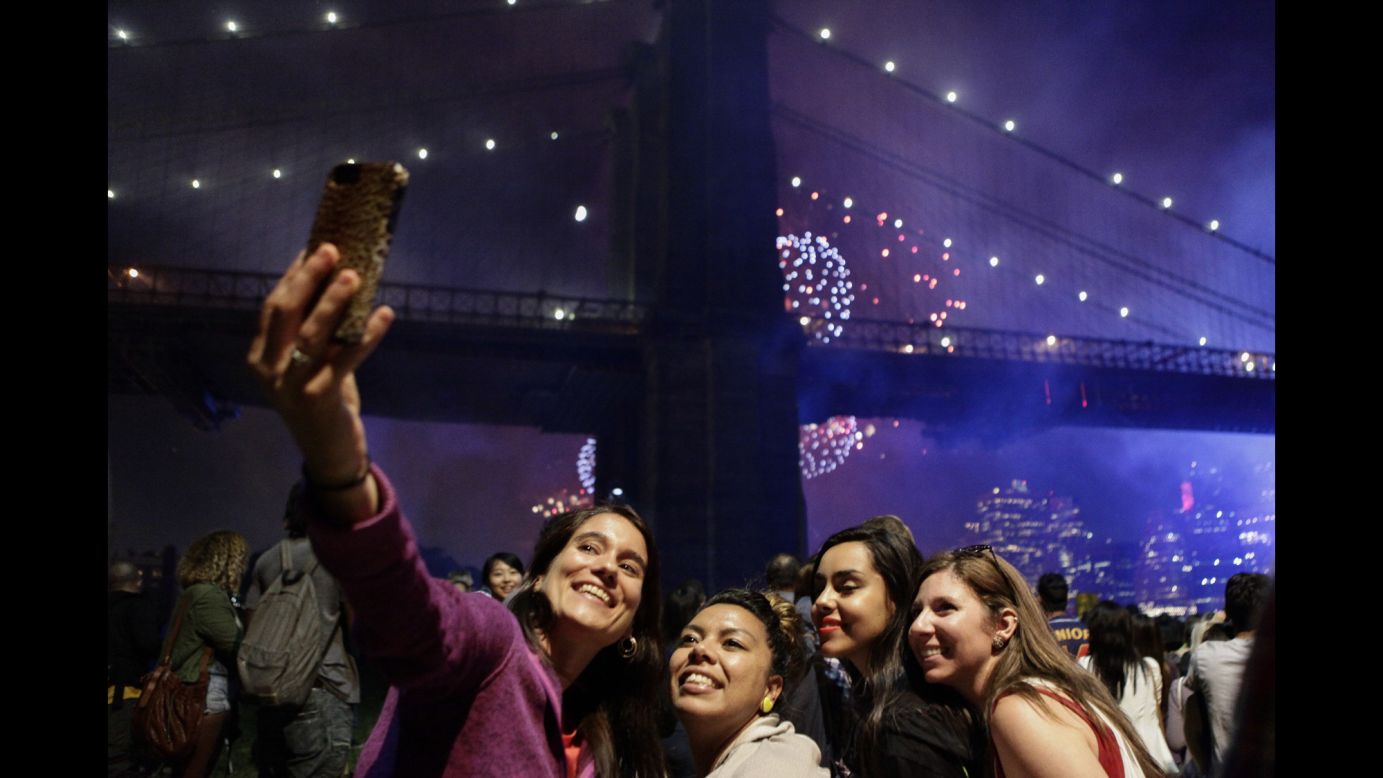 People pose for a photo Friday, July 4, as fireworks are seen near the Brooklyn Bridge in New York. The Fourth of July fireworks show returned to the East River for the first time since 2008.