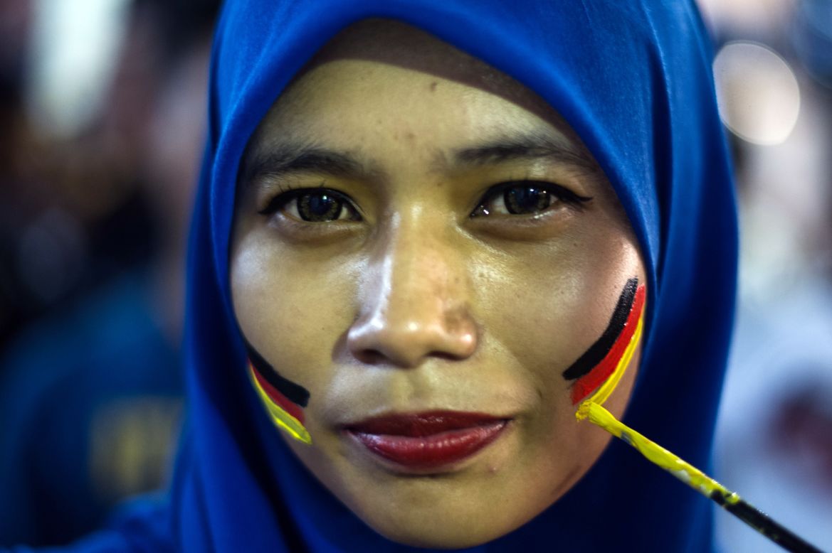 Una hincha malasia con una mirada esperanzadora que se deja pintar las mejillas con la bandera de Alemania.