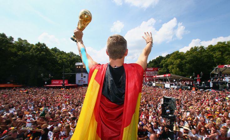 Bastian Schweinsteiger channels Superman with a cape made out of the German flag as he lifts the trophy in front of a packed Berlin crowd.