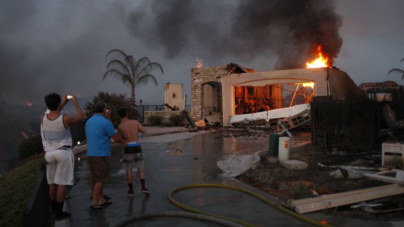 Residents photograph the burning ruins of their home, which was destroyed in a wildfire in Carlsbad, California, in May 2014.
