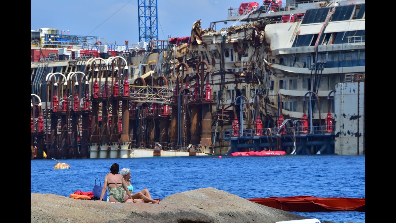 People sunbathe on rocks facing the wrecked <a href="http://www.cnn.com/2013/07/18/europe/gallery/costa-concordia/index.html" target="_blank">Costa Concordia</a> cruise ship on Sunday, July 13, off the shore of Giglio, Italy. Two and a half years after it ran aground, crews began to raise the ship from the seabed on July 14.