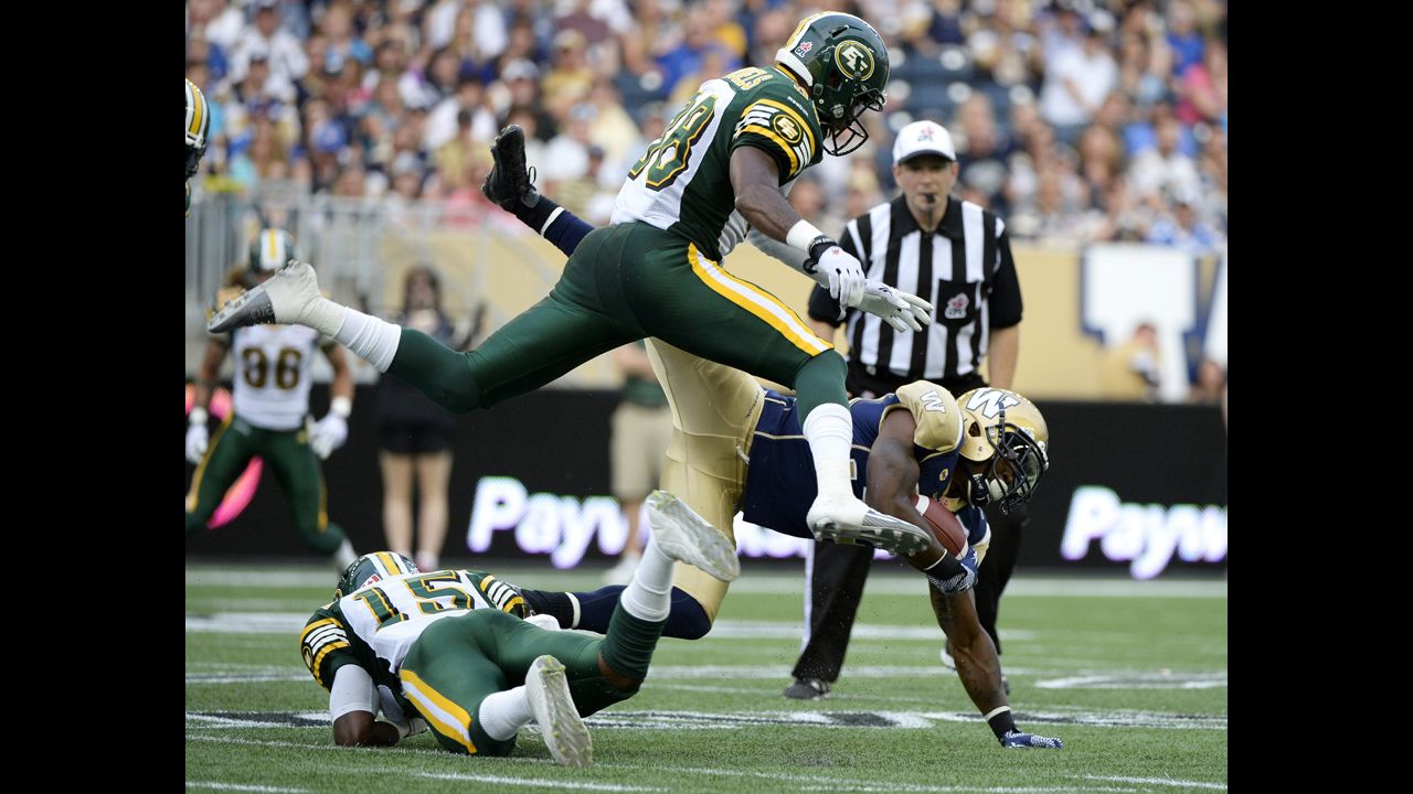 Nic Grigsby of the Winnipeg Blue Bombers is tackled by Edmonton's Chris Rwabukamba, left, and Eric Samuels during a CFL football game Thursday, July 17, in Winnipeg, Manitoba.