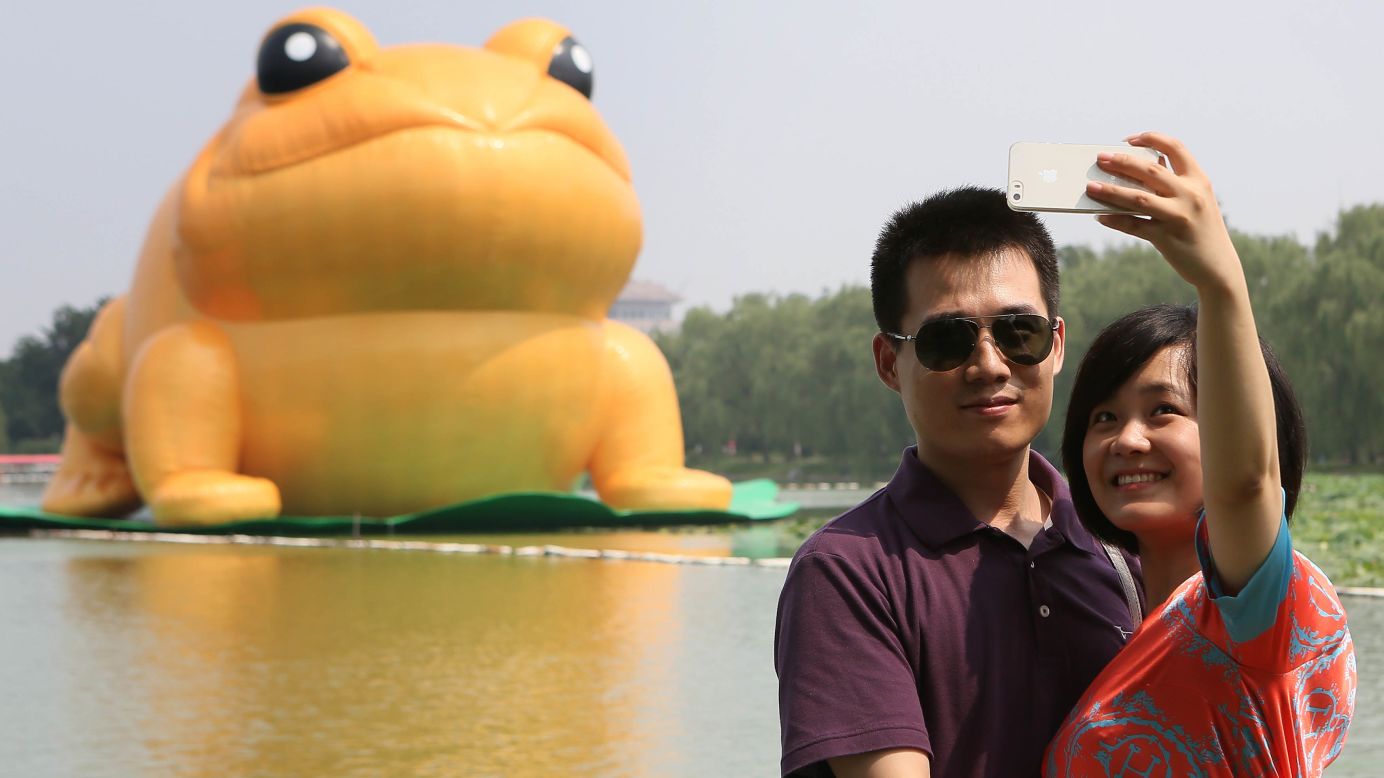 People take photos in front of a large golden fabric frog Saturday, July 19, in Beijing's Yuyuantan Park. The frog, which is 22 meters (72 feet) tall, is based on the golden frog that symbolizes luck and is thought to bring wealth and fortune in traditional Chinese culture.