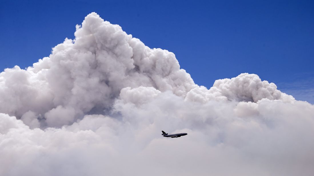 A plane is dwarfed by the tip of a rising smoke cloud as it prepares to drop fire retardant over a wildfire near Carlton, Washington, on Saturday, July 19.