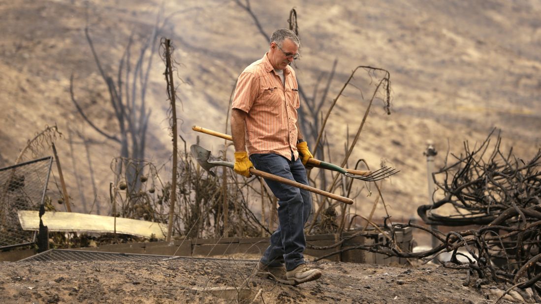 David Burdick walks past the smoldering remains of his niece's home after sifting through the rubble July 18 in Pateros.