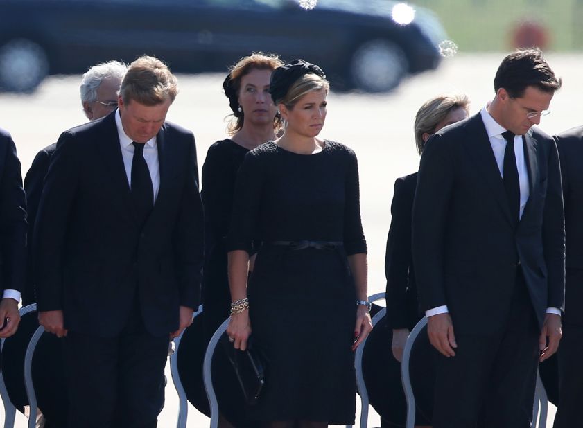 Dutch King Willem-Alexander, Queen Maxima and Prime Minister Mark Rutte stand together as unidentified bodies are transferred to hearses.