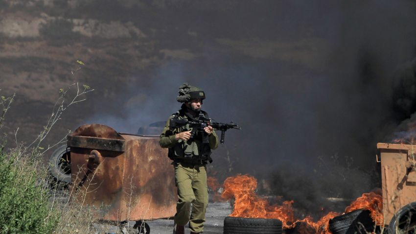 An armed Israeli soldier walks past burning tires during clashes with Palestinians at the gates of Beit El Jewish settlement in the Israel occupied West Bank near Ramallah following a march organised by the Palestinian Islamic movement Hamas towards the settlement on July 25, 2014. Five Palestinians were killed in the West Bank on July 25, 2014 in two separate incidents involving both Israeli troops and Israeli settlers, Palestinian security sources told AFP.    AFP PHOTO / ABBAS MOMANI        (Photo credit should read ABBAS MOMANI/AFP/Getty Images)