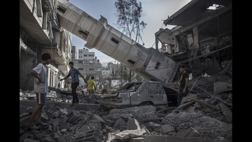 Palestinians walk under the collapsed minaret of a destroyed mosque in Gaza City on Wednesday, July 30.