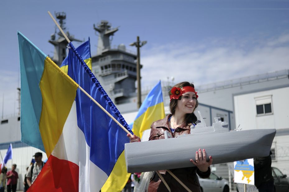 A woman holds a French and Ukrainian flag and a model of a boat as she demonstrates in front of the warship in Saint-Nazaire.