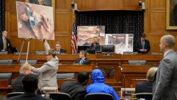 Image #: 31125448    Photographs of victims of the Assad regime are displayed as a Syrian Army defector known as "Caesar", center, appears in disguise to speak before the House Foreign Affairs Committee at a briefing called "Assad's Killing Machine Exposed: Implications for U.S. Policy" concerning the Assad regime, on Capitol Hill, Washington, D.C., Thursday, July 31, 2014. "Caesar" was apparently a witness to Bashar al-Assad's brutality and as smuggled more than 50,000 photographs depicting the torture and execution of more then 10,000 dissidents. ()     The Washington Times /Landov