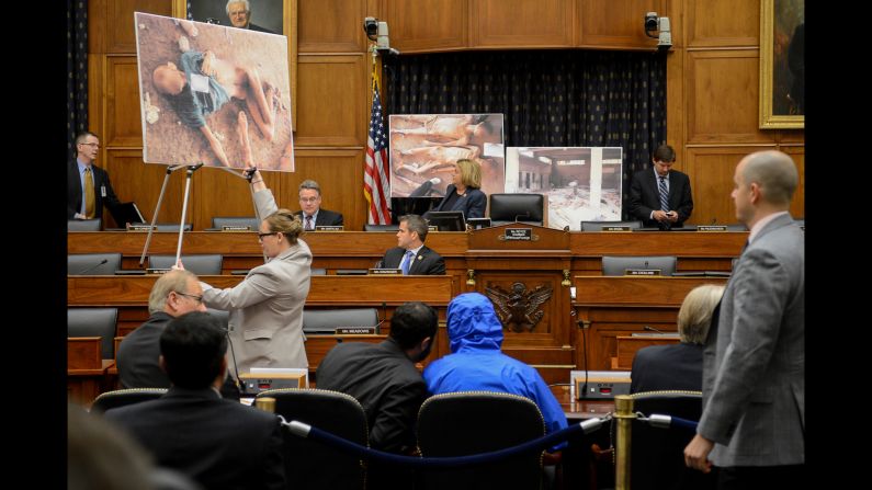 Photographs of victims of the Bashar al-Assad regime are displayed as a Syrian Army defector known as "Caesar," center, appears in disguise to speak before the House Foreign Affairs Committee. The briefing is called "Assad's Killing Machine Exposed: Implications for U.S. Policy" in Washington on Thursday, July 31. "Caesar" was apparently a witness to al-Assad's brutality and has smuggled more than 50,000 photographs depicting the torture and execution of more than 10,000 dissidents. 