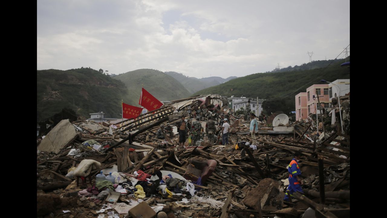 A rescuer walks past paramilitary policemen searching for survivors at a destroyed house in Longtoushan on August 5.