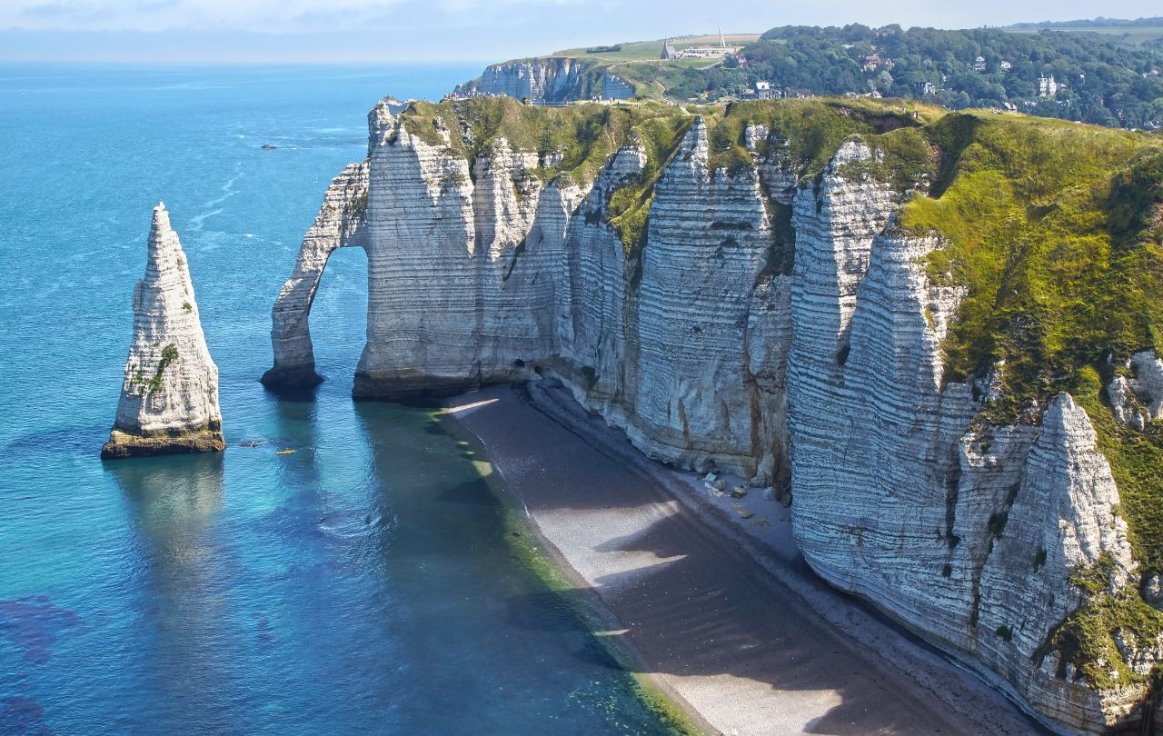 Natural arches have emerged from the chalky cliffs of Etretat, France, a scene that inspired Claude Monet and other impressionists. A wide beach fronts the resort town beyond this dramatic formation.