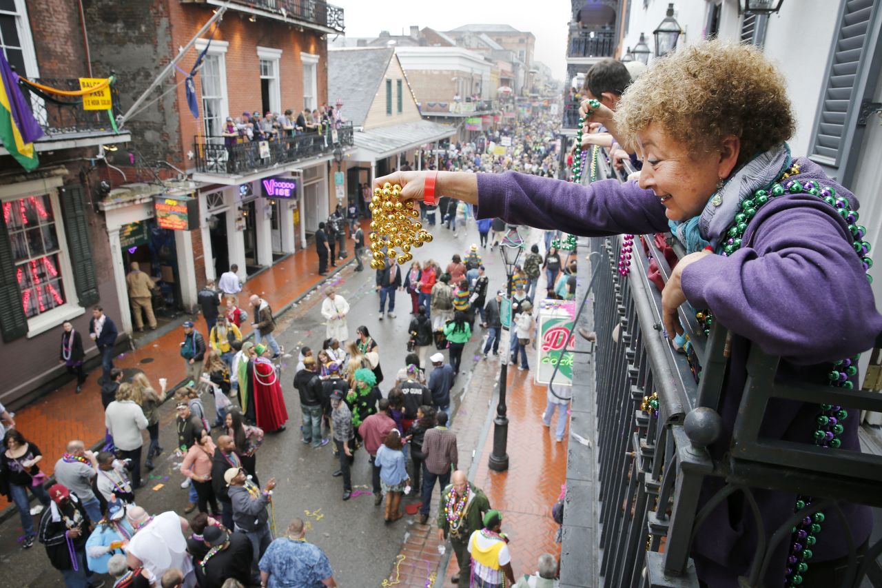 A Mardi Gras reveler dangles a pair of beads off of a balcony on Bourbon Street in New Orleans.