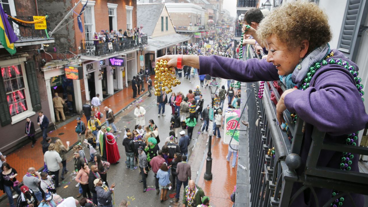 A Mardi Gras reveler dangles a pair of beads off of a balcony on Bourbon Street in New Orleans.