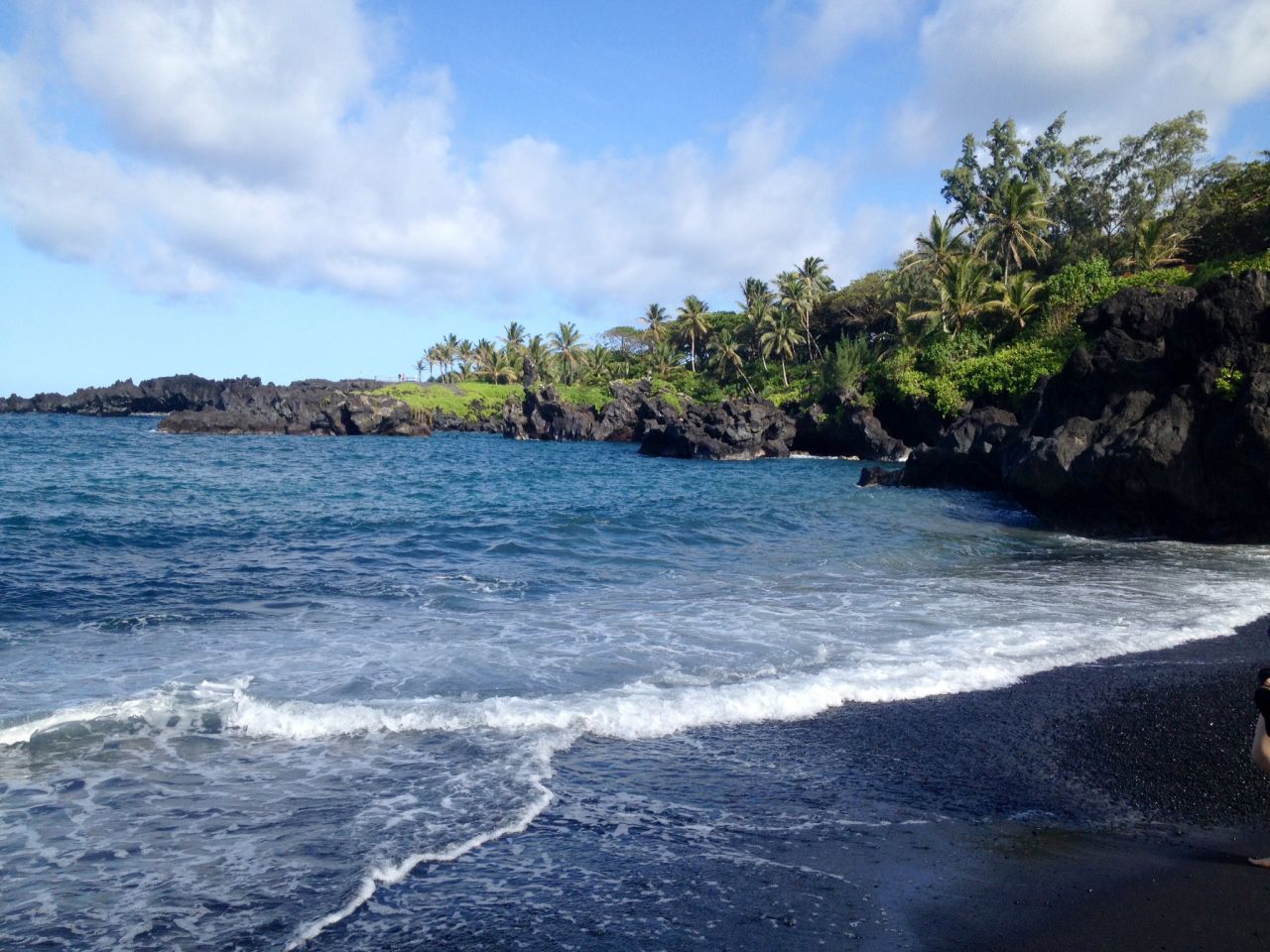 Low volcanic cliffs surround a small black sand beach at Waianapanapa State Park, off the famous Hana Highway in Maui.