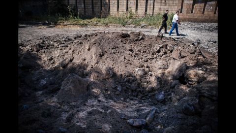 Men walk past a bomb crater in Donetsk on August 6.
