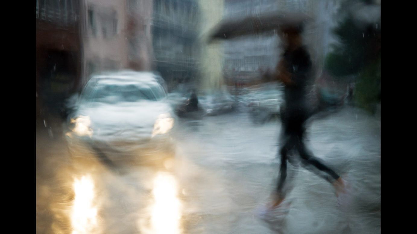 A woman with an umbrella crosses a street in Hanover, Germany, on Monday, August 4. This photo was taken through the rain-drenched window of a car.
