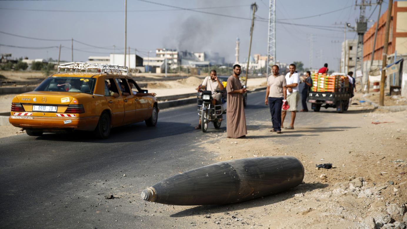 Palestinians look at an unexploded Israeli shell that landed on the main road outside the Gaza town of Deir al-Balah on Friday, August 1.