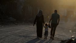 :Sammy Al-Sheikh (R) and his wife Maha (L) hold hands with their three-year-old daughter Assil as they walk past destroyed houses in the devastated neighbourhood of Shejaiya in Gaza City on August 7, 2014. Sammy who lives and works in Gaza City expressed hopes for peace and said peace would allow him to return to work. Fears rose that the Gaza conflict could resume as a temporary ceasefire entered a final 12-hour stretch and Palestinians accused Israel of stalling at truce talks in Cairo. AFP PHOTO/ROBERTO SCHMIDT (Photo credit should read
