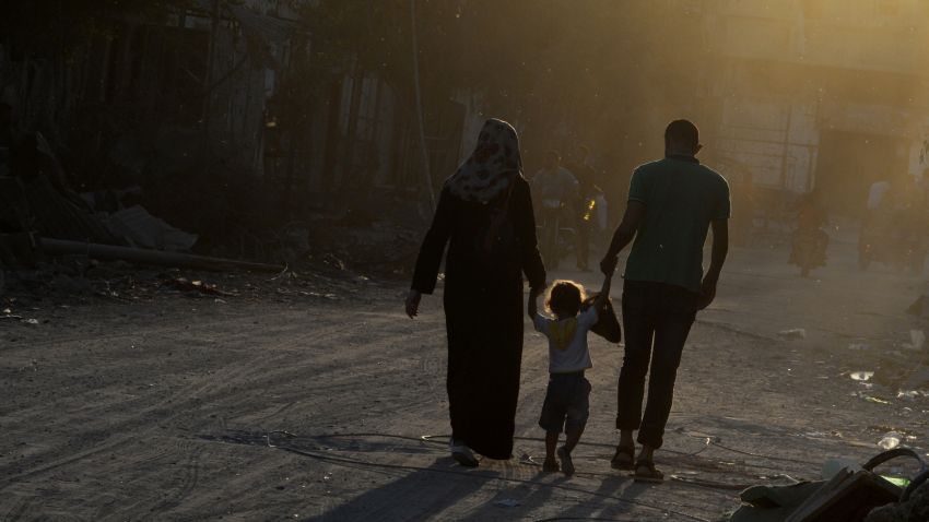 :Sammy Al-Sheikh (R) and his wife Maha (L) hold hands with their three-year-old daughter Assil as they walk past destroyed houses in the devastated neighbourhood of Shejaiya in Gaza City on August 7, 2014. Sammy who lives and works in Gaza City expressed hopes for peace and said peace would allow him to return to work. Fears rose that the Gaza conflict could resume as a temporary ceasefire entered a final 12-hour stretch and Palestinians accused Israel of stalling at truce talks in Cairo. AFP PHOTO/ROBERTO SCHMIDT (Photo credit should read 