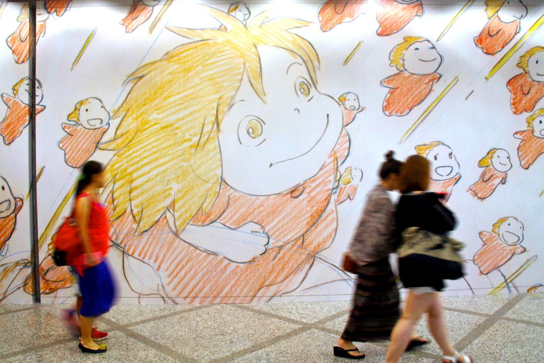 Visitors at a Studio Ghibli exhibit in Hong Kong walk by a wall of artwork.