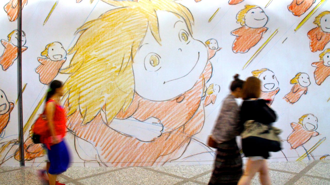 Visitors at a Studio Ghibli exhibit in Hong Kong walk by a wall of artwork.