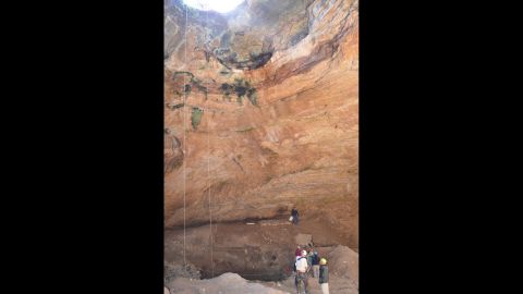 Researchers stand below the entrance to the cave. 
