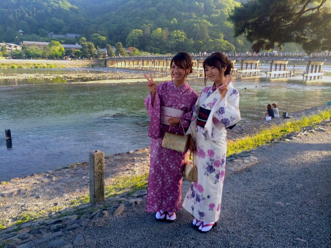 Kimono-clad Japanese tourists pose in front of Arashiyama's Togetsukyo Bridge. 